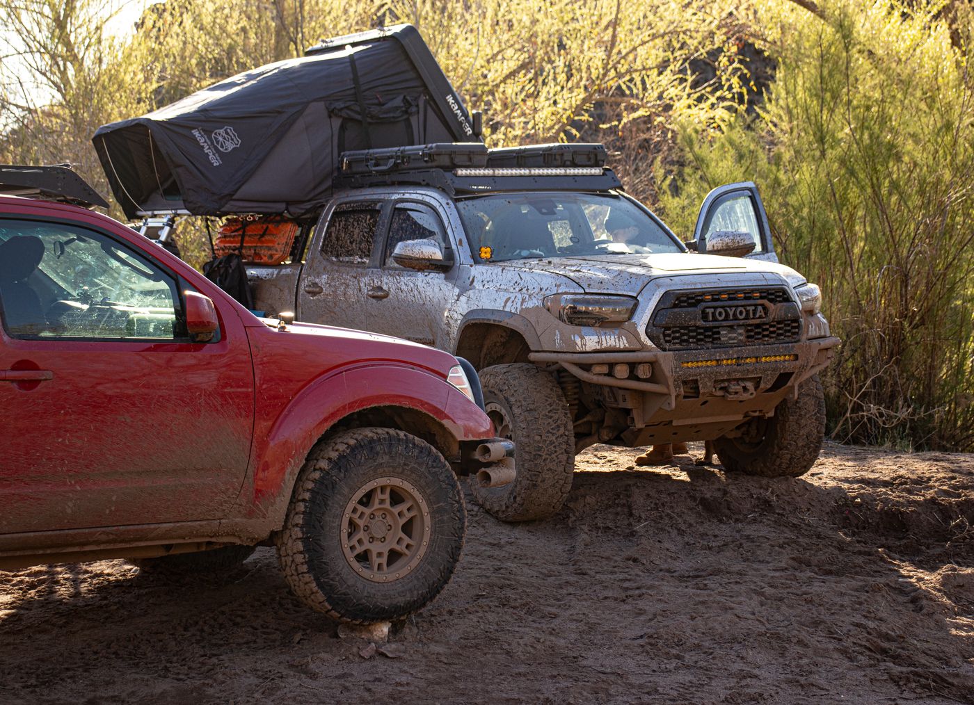 Two trucks working up a muddy trail in low sun
