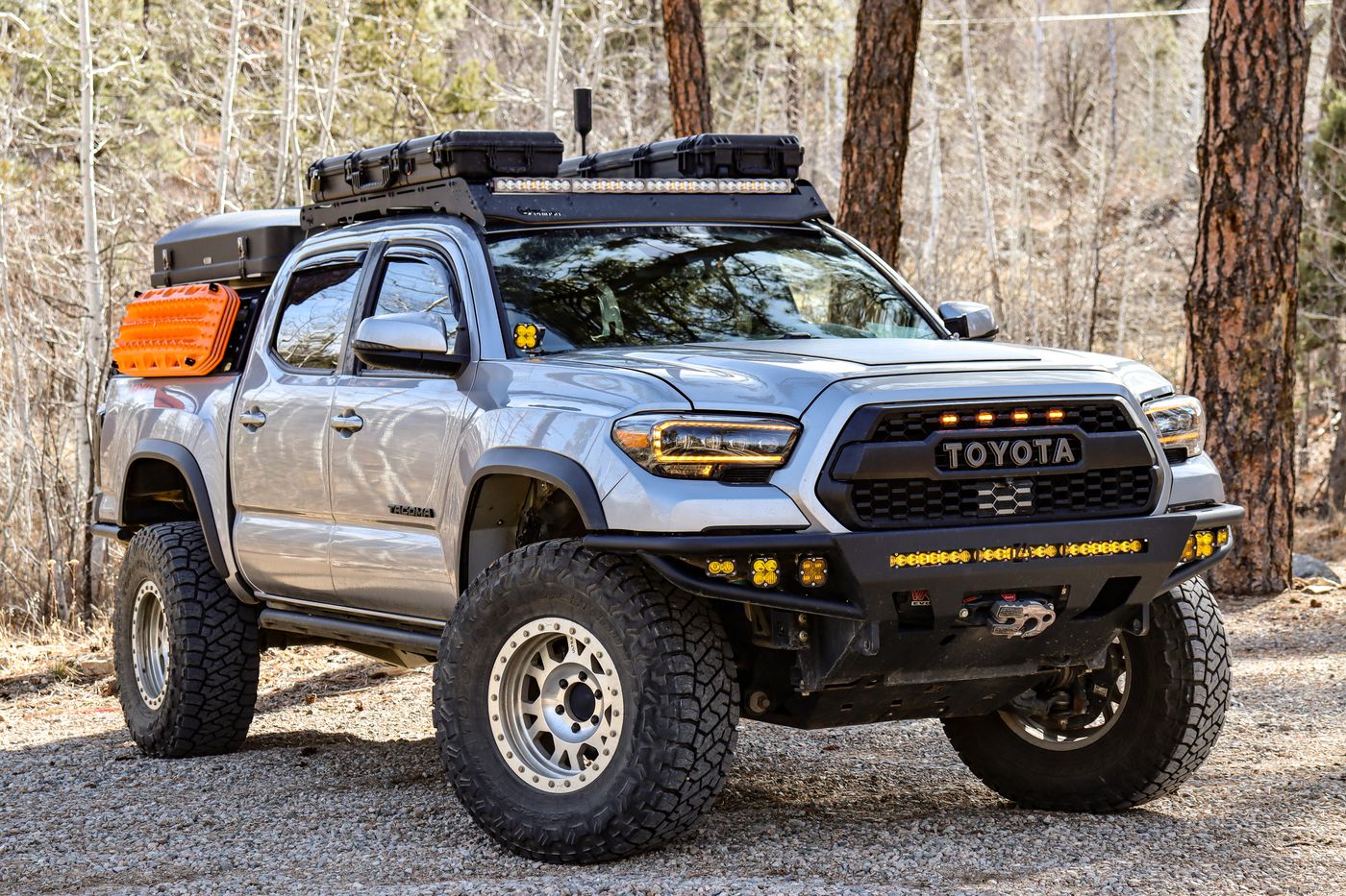 Front three-quarter view of the built Tacoma — bumper, lights, roof rack, and recovery gear visible