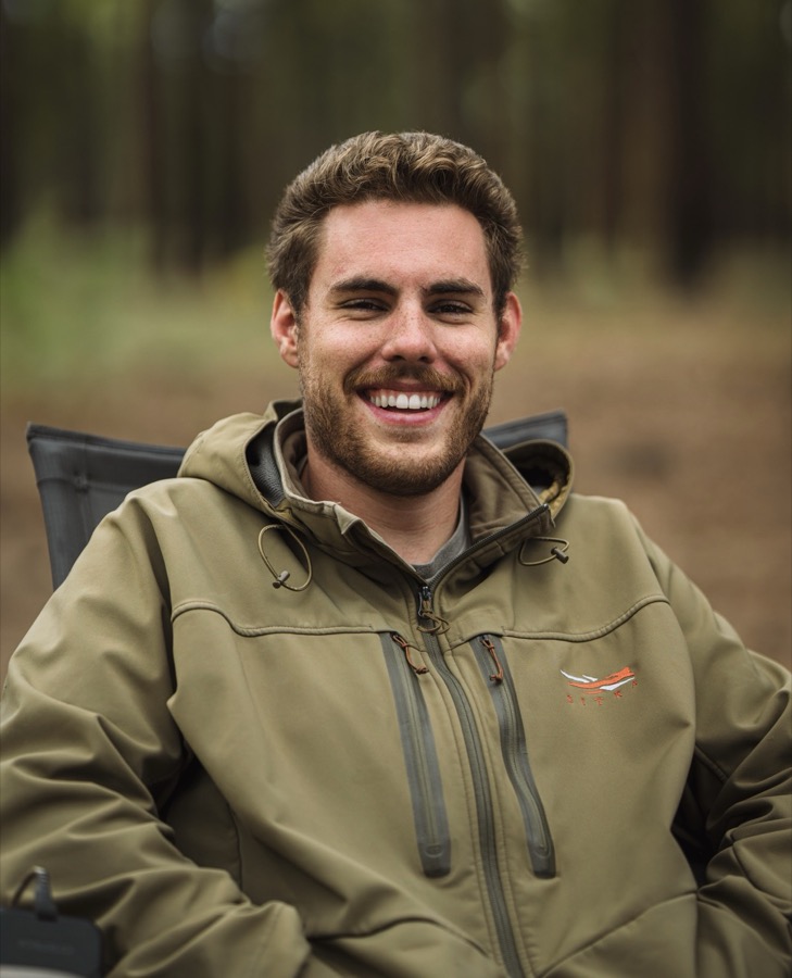 Luke Lollar smiling in a camp chair in a pine forest